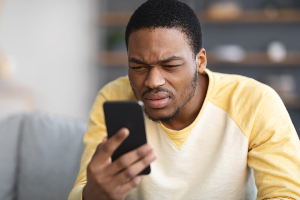 Young male squinting while looking at his mobile phone screen at home.